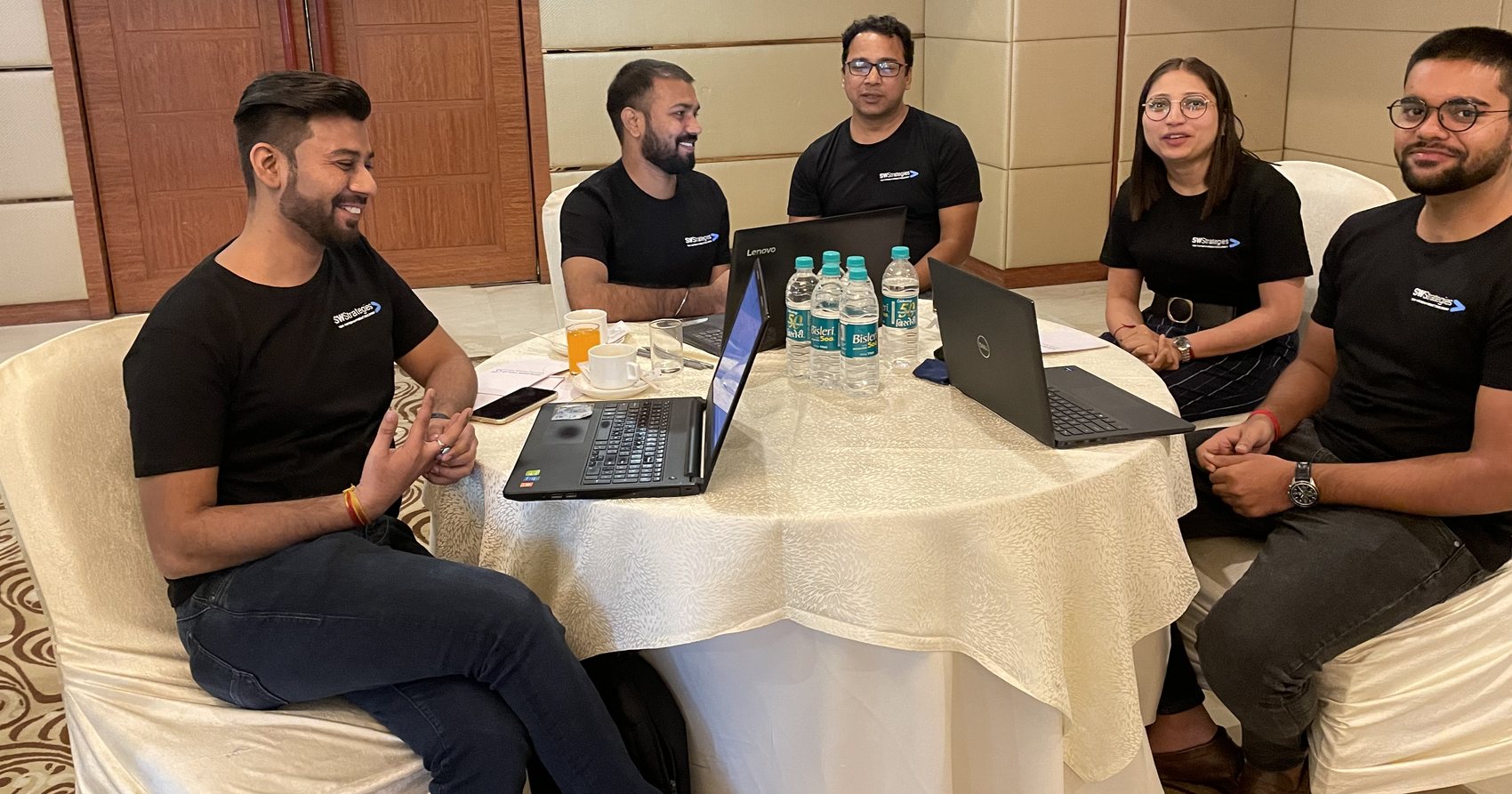Five members of the SWStrategies team working together around a table with laptops open